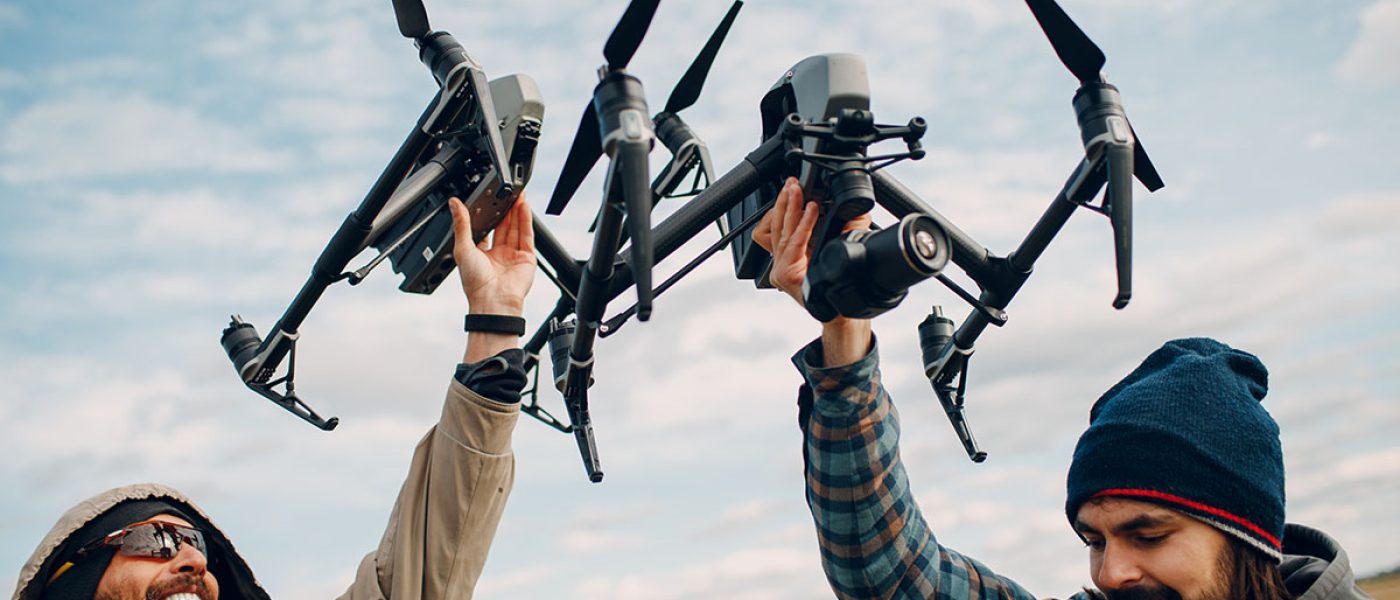 Two men pilots holding quadcopter drone in hands at outside field