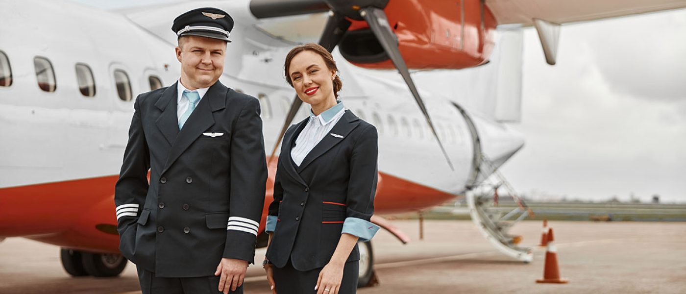 Pilot and stewardess on runway near airplane jet. Modern passenger plane. Smiling european man and woman wear uniform and looking at camera. Civil commercial aviation. Air travel concept